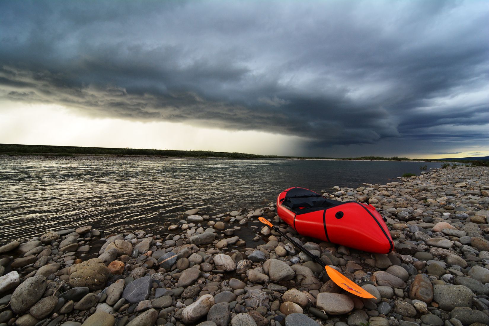 Red packraft on a gravel bar under a stormy sky in Alaska